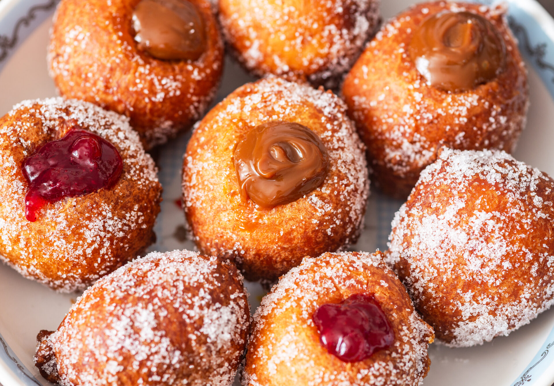 A plate of sugar-coated doughnuts filled with either chocolate or red fruit jam.